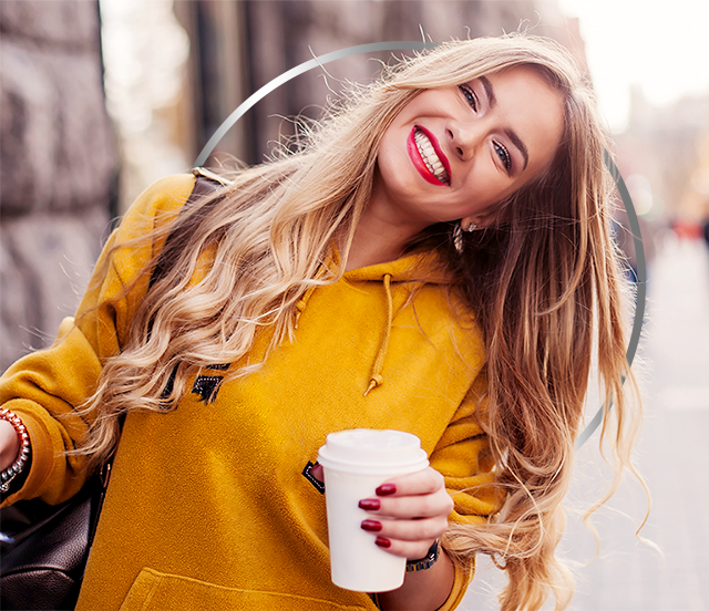 Vesela mlada ženska v rumenem puloverju s kapuco drži papirnat lonček za kavo
